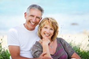 An older couple wearing affordable dental implants smiles with confidence.