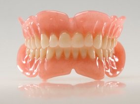 A complete set of removable dentures with a pink acrylic base and white teeth.